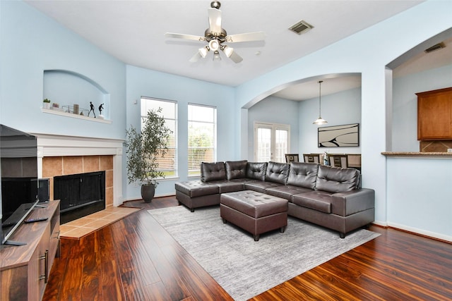 living room featuring dark hardwood / wood-style floors, ceiling fan, and a tiled fireplace