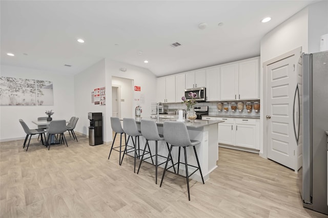 kitchen with a center island with sink, tasteful backsplash, light hardwood / wood-style floors, white cabinetry, and stainless steel appliances