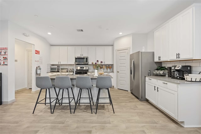 kitchen featuring white cabinets, light wood-type flooring, stainless steel appliances, and tasteful backsplash