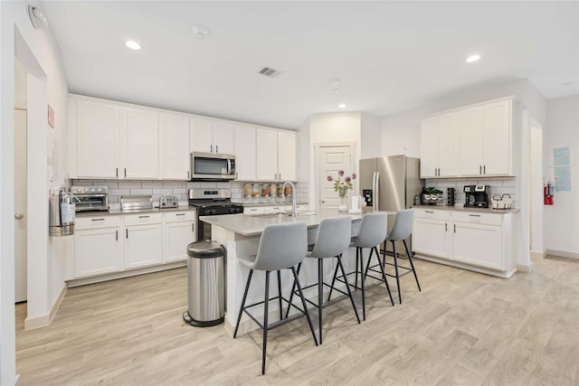 kitchen with white cabinets, an island with sink, appliances with stainless steel finishes, and a breakfast bar area