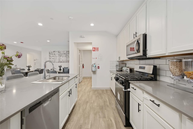 kitchen with appliances with stainless steel finishes, light wood-type flooring, tasteful backsplash, sink, and white cabinets