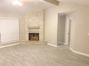 unfurnished living room with light hardwood / wood-style flooring, vaulted ceiling with beams, a fireplace, and ceiling fan