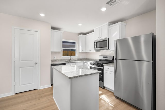 kitchen with stainless steel appliances, white cabinetry, and light hardwood / wood-style floors