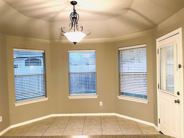 unfurnished dining area with a tray ceiling and light tile patterned flooring