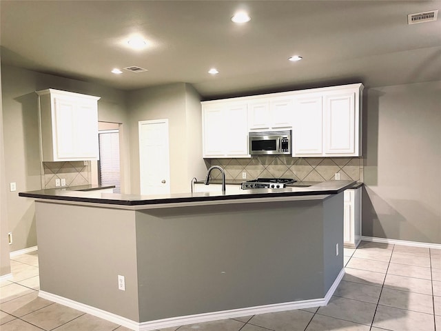 kitchen featuring tasteful backsplash, sink, a center island with sink, white cabinets, and light tile patterned flooring