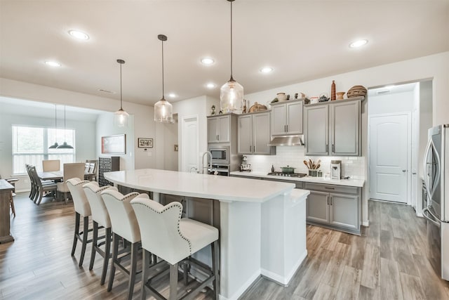 kitchen featuring stainless steel appliances, backsplash, a large island with sink, decorative light fixtures, and a kitchen bar