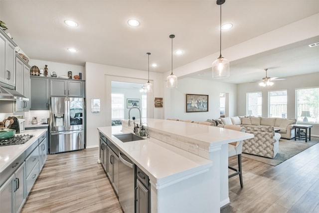 kitchen featuring pendant lighting, a kitchen island with sink, sink, gray cabinets, and appliances with stainless steel finishes