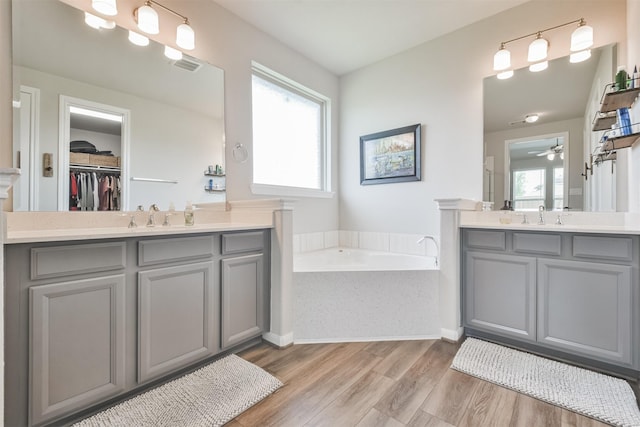 bathroom with vanity, hardwood / wood-style flooring, a wealth of natural light, and tiled tub