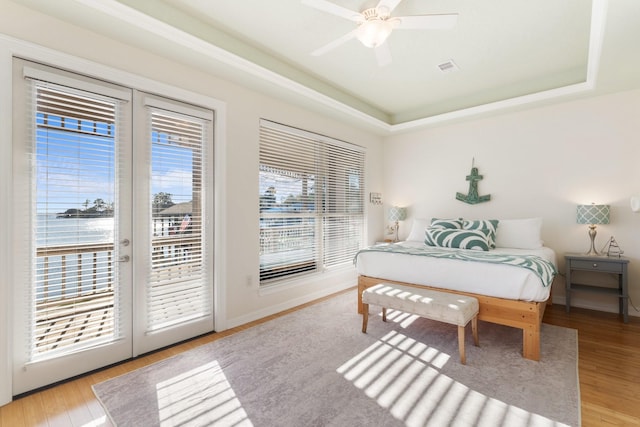 bedroom with a raised ceiling, access to exterior, ceiling fan, and multiple windows