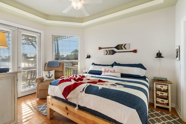 bedroom with hardwood / wood-style floors, ceiling fan, and a tray ceiling