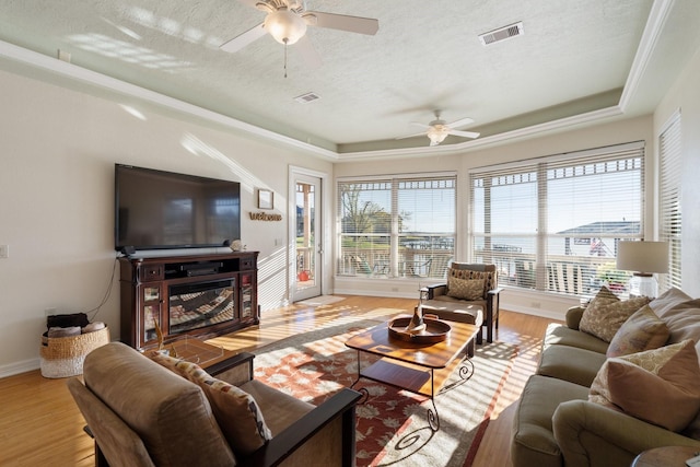 living room featuring a textured ceiling, light wood-type flooring, a tray ceiling, and ceiling fan