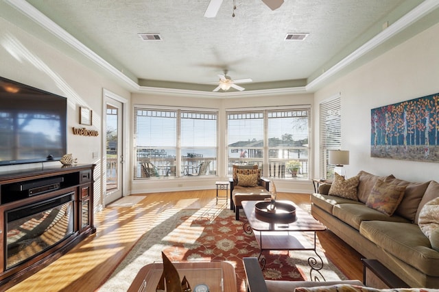 living room with ceiling fan, light hardwood / wood-style flooring, a textured ceiling, and a tray ceiling