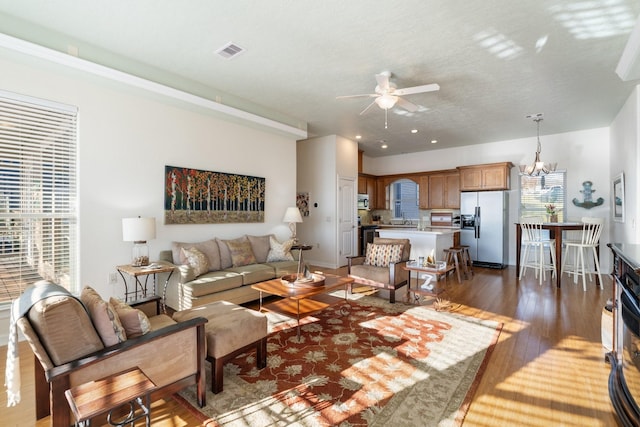 living room featuring ceiling fan with notable chandelier and dark wood-type flooring