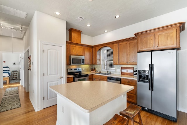 kitchen with a center island, sink, stainless steel appliances, light hardwood / wood-style flooring, and decorative backsplash