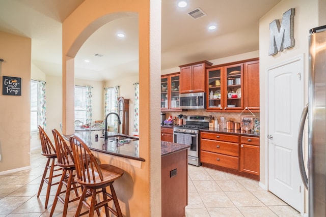 kitchen featuring dark stone counters, a breakfast bar, stainless steel appliances, sink, and light tile patterned flooring