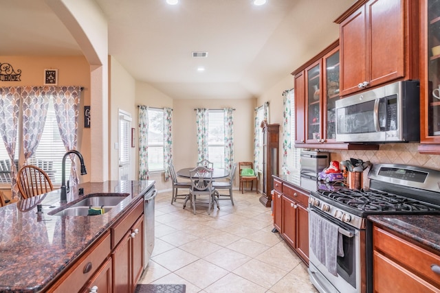 kitchen featuring lofted ceiling, stainless steel appliances, dark stone countertops, and sink