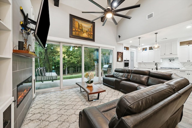 living room featuring high vaulted ceiling, sink, ceiling fan, light hardwood / wood-style floors, and a tiled fireplace