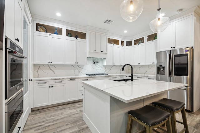 kitchen with white cabinets, light stone counters, an island with sink, and appliances with stainless steel finishes