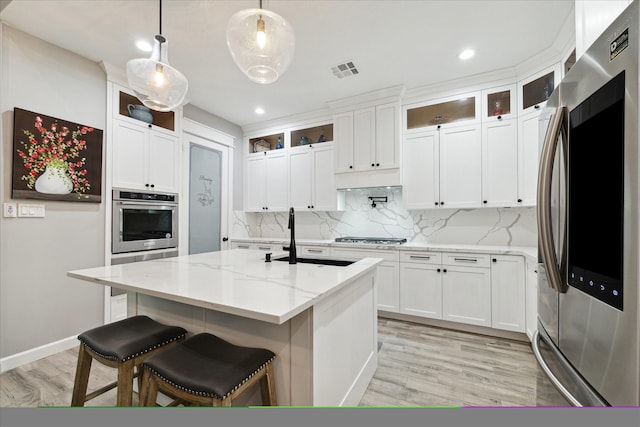 kitchen featuring light stone countertops, hanging light fixtures, stainless steel appliances, a center island with sink, and white cabinets