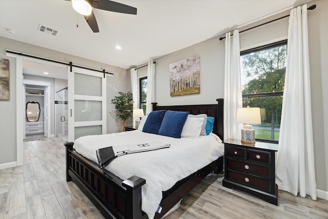 bedroom with a barn door, light hardwood / wood-style flooring, and ceiling fan