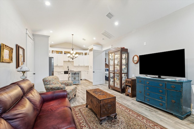 living room with sink, lofted ceiling, light hardwood / wood-style flooring, and an inviting chandelier