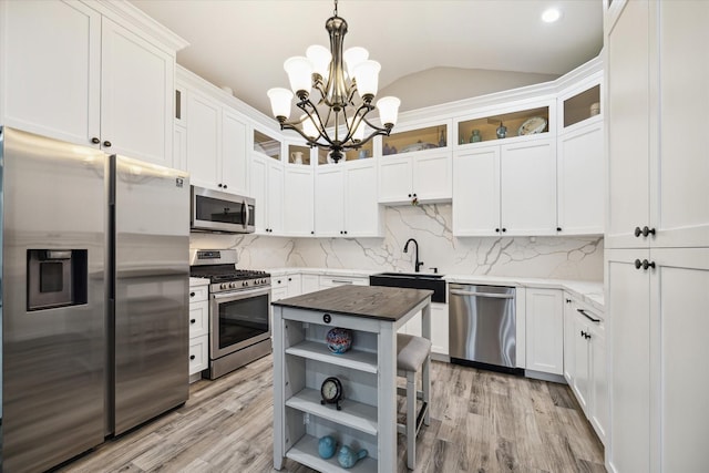 kitchen with appliances with stainless steel finishes, vaulted ceiling, pendant lighting, a chandelier, and white cabinetry