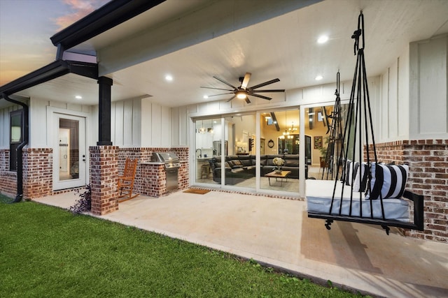 patio terrace at dusk featuring area for grilling, ceiling fan, and exterior kitchen