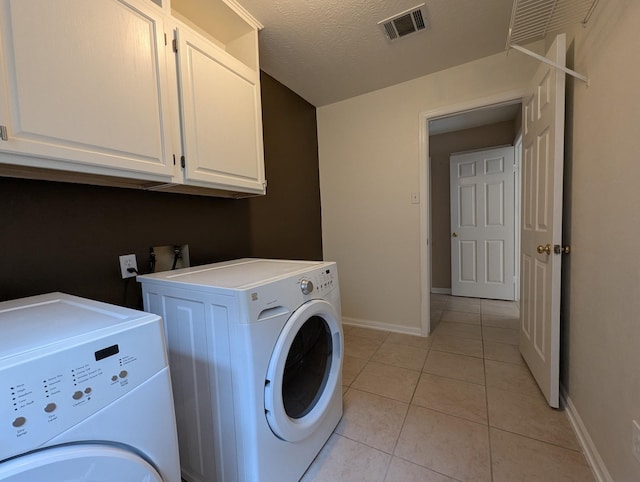 laundry area with washing machine and dryer, cabinets, light tile patterned floors, and a textured ceiling