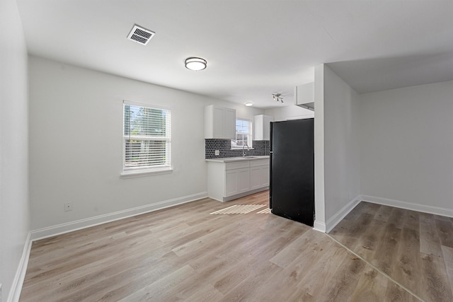 kitchen featuring light hardwood / wood-style floors, black fridge, white cabinetry, and backsplash