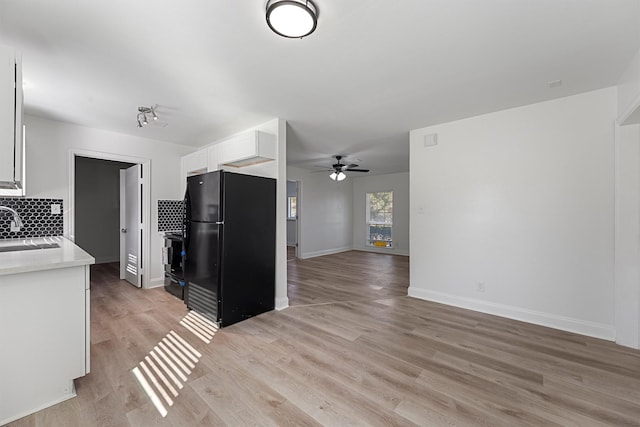 kitchen with decorative backsplash, light wood-type flooring, sink, black appliances, and white cabinets