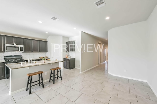 kitchen featuring tasteful backsplash, light stone counters, a center island with sink, and range