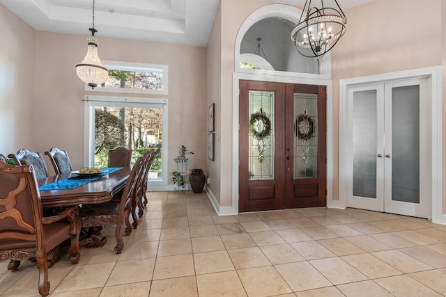 tiled foyer entrance with an inviting chandelier, a raised ceiling, a high ceiling, and french doors