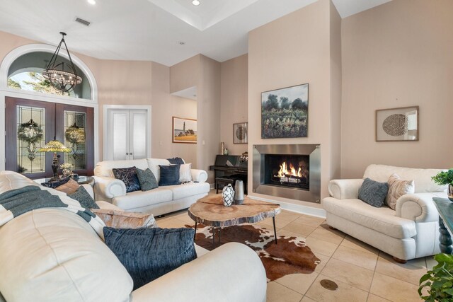 tiled living room featuring french doors, a towering ceiling, and a notable chandelier