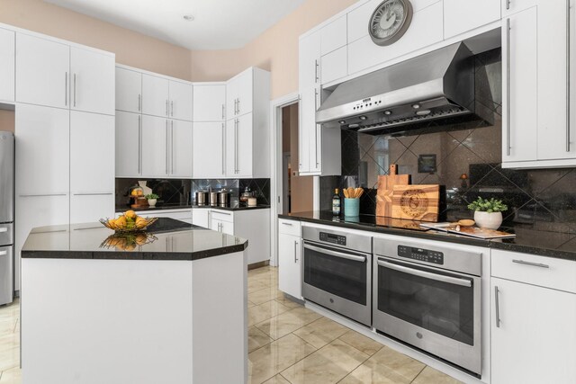 kitchen with decorative backsplash, wall chimney exhaust hood, stainless steel appliances, a center island, and white cabinetry