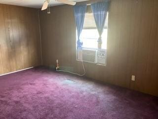 unfurnished room with wooden walls, carpet floors, and ceiling fan