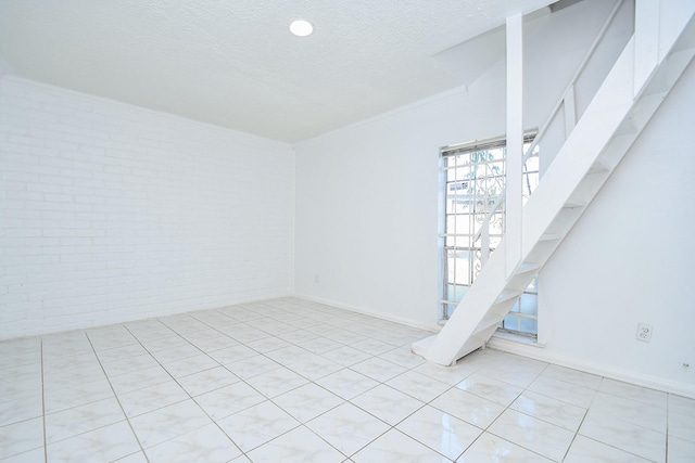 empty room with a textured ceiling, ornamental molding, and brick wall