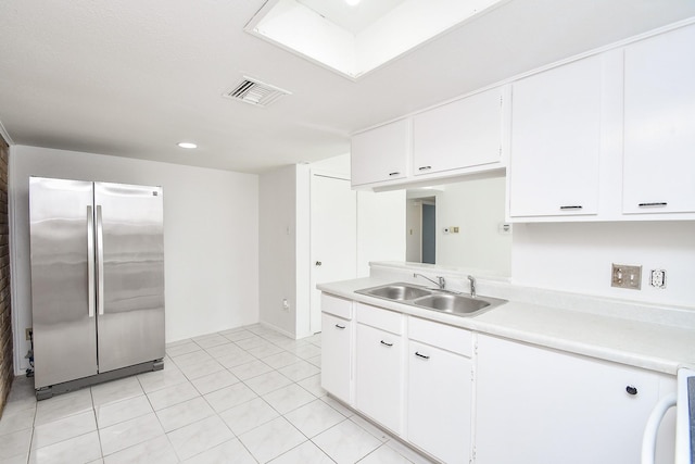 kitchen with stainless steel refrigerator, sink, white cabinets, and light tile patterned floors