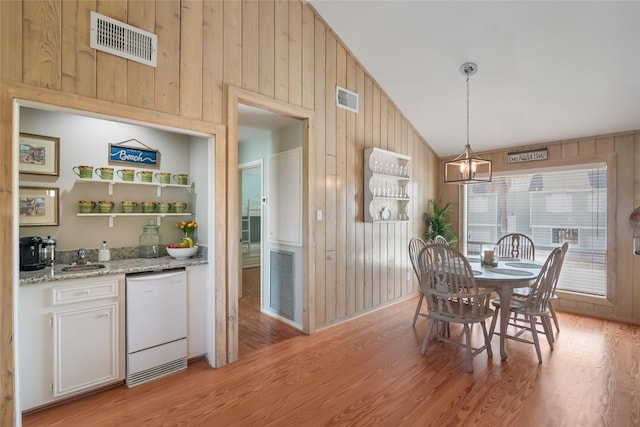 dining space featuring sink, an inviting chandelier, light hardwood / wood-style flooring, lofted ceiling, and wooden walls