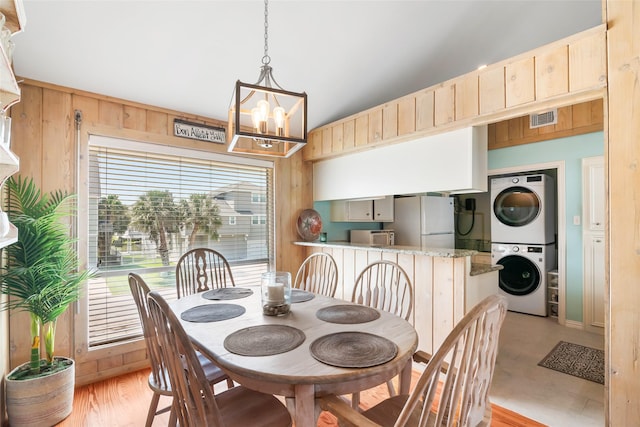 dining space with wood walls, stacked washer and clothes dryer, and a notable chandelier