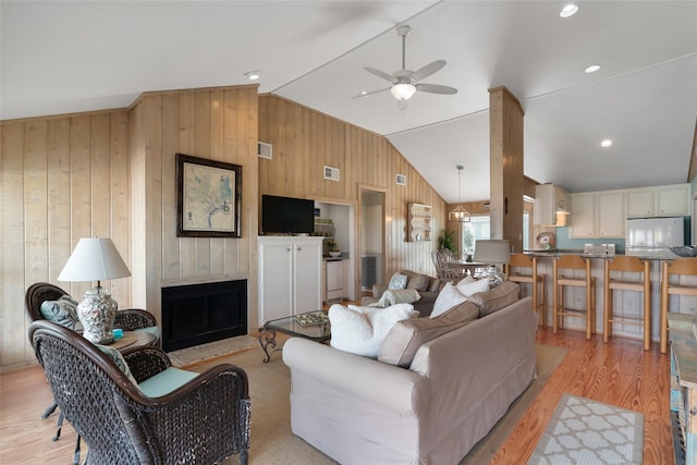 living room with light hardwood / wood-style floors, vaulted ceiling, ceiling fan, and wood walls