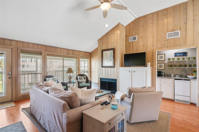 living room with ceiling fan, wood walls, light wood-type flooring, and vaulted ceiling