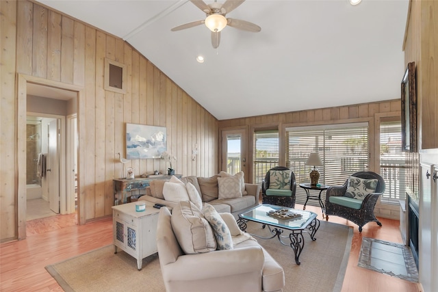 living room with wood walls, light hardwood / wood-style flooring, ceiling fan, and vaulted ceiling