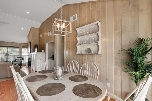 dining room featuring wooden walls, a notable chandelier, lofted ceiling, and hardwood / wood-style flooring