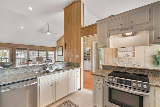 kitchen with sink, wooden walls, ceiling fan, light stone countertops, and stainless steel appliances