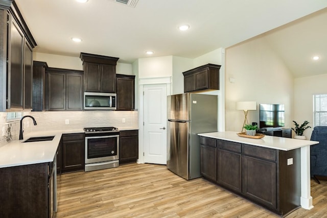 kitchen with dark brown cabinetry, sink, light hardwood / wood-style floors, decorative backsplash, and appliances with stainless steel finishes