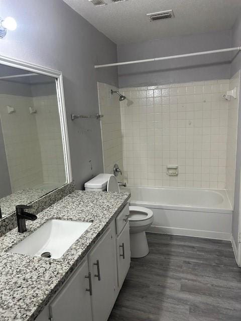 full bathroom with tiled shower / bath combo, wood-type flooring, a textured ceiling, toilet, and vanity