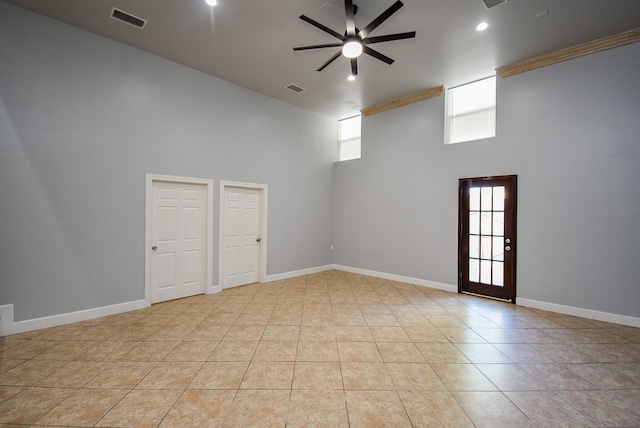 tiled spare room with a wealth of natural light, ceiling fan, and a towering ceiling