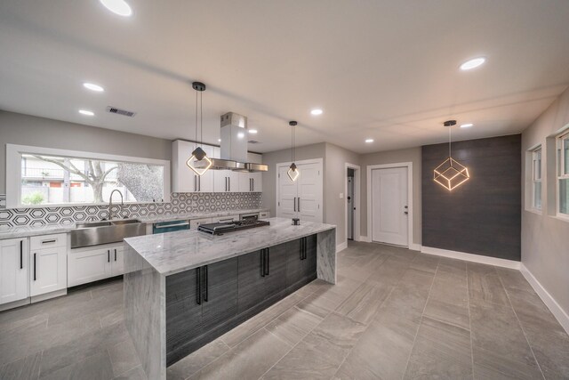 kitchen featuring white cabinetry, sink, light stone countertops, decorative light fixtures, and a kitchen island