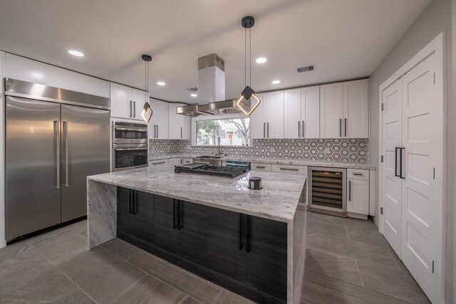 kitchen featuring stainless steel appliances, beverage cooler, decorative light fixtures, white cabinetry, and a kitchen island