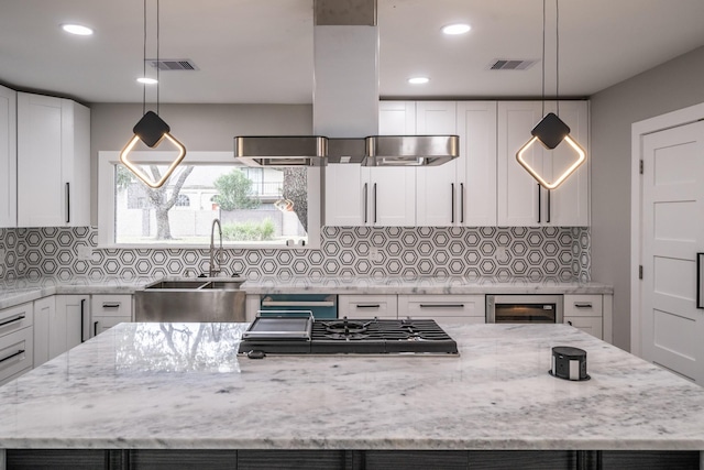 kitchen with light stone counters, a center island, white cabinets, and hanging light fixtures